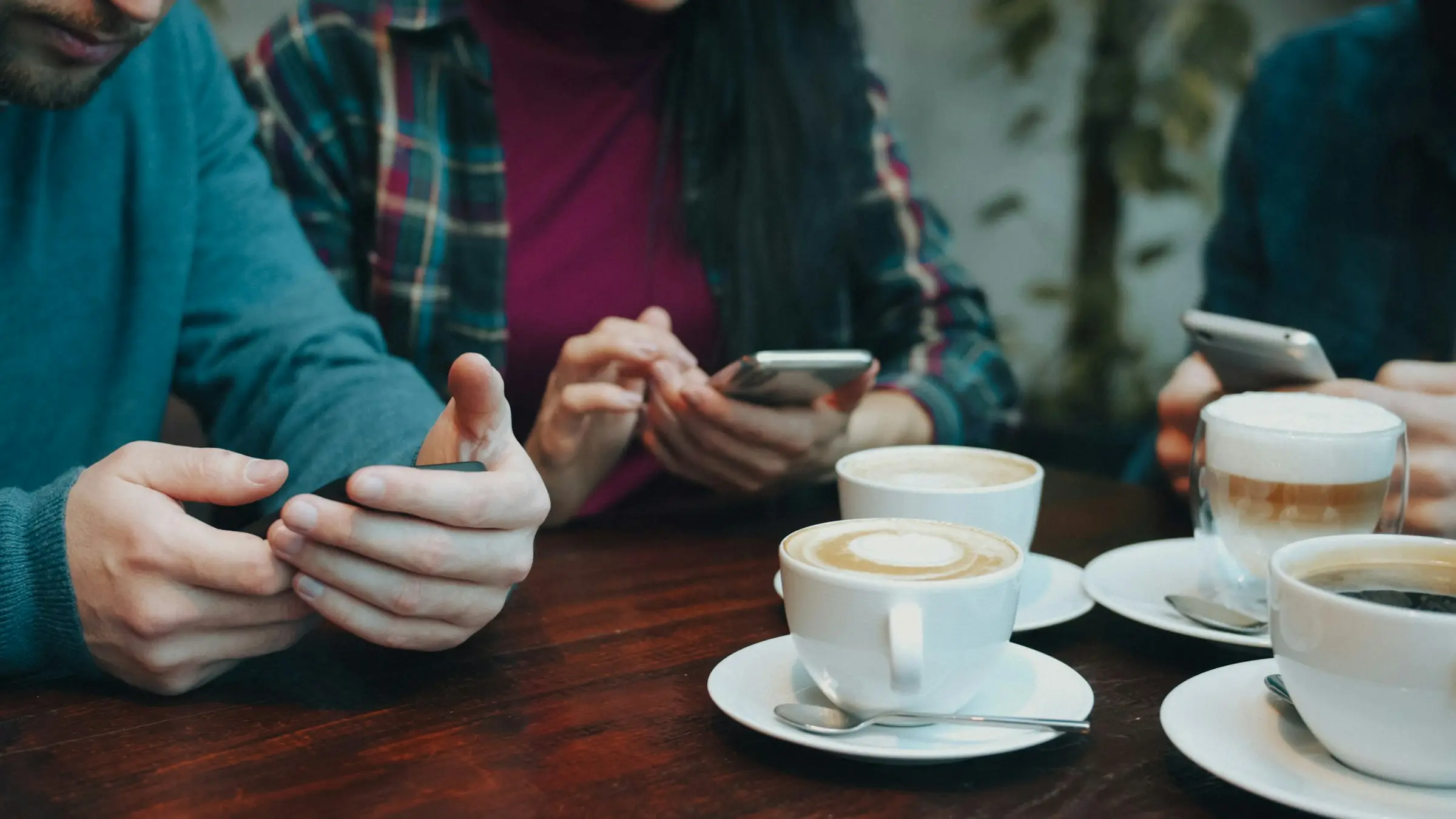 People checking their phones over coffee at a wooden table.